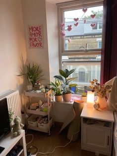 a living room filled with lots of plants next to a large window covered in valentine's day decorations