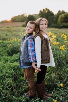 two children are standing in a field with sunflowers and one is wearing a vest