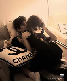 two young women sitting on a couch with chanel pillow in front of their faces