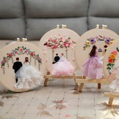 three hand embroidered dolls are sitting in front of two hoop - shaped frames with flowers on them