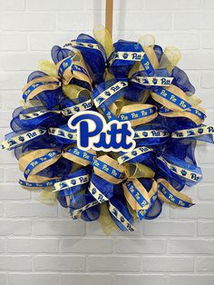 a blue and gold wreath with the word pitt on it hanging from a brick wall