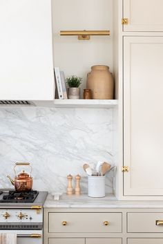 a kitchen with white cabinets and marble counter tops, gold pulls on the oven hood