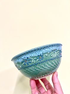 a hand holding a small blue bowl in it's left hand, against a white background