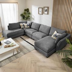 a living room with a large sectional couch and coffee table in it, along with potted plants