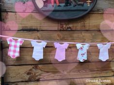 baby ones hanging on a clothes line in front of a wooden wall with a mirror