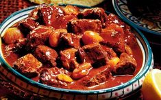 a bowl filled with meat and sauce next to rice on a tablecloth covered table