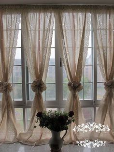 a vase filled with flowers sitting next to two windows covered in sheer curtaines and bowknots