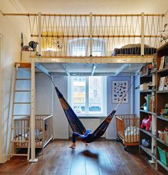 a person laying in a hammock on top of a wooden floor next to a book shelf