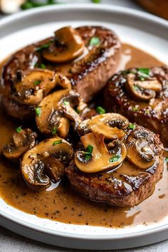 two steaks with mushrooms and gravy on a plate