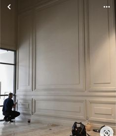 a man sitting on the floor in front of a wall with white paneling and paint