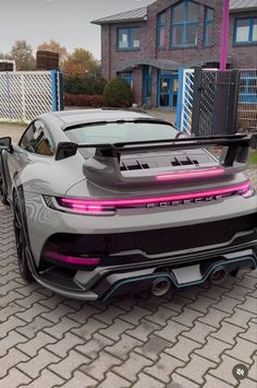 a grey sports car parked in front of a brick building with pink lights on it