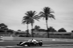 a man driving a race car on a track with palm trees in the back ground