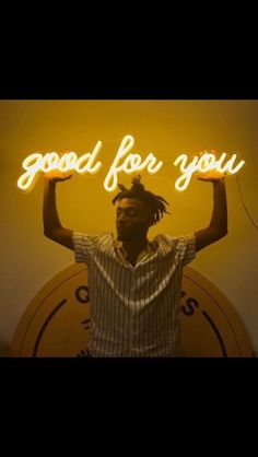 a man standing in front of a neon sign with his hands up and the words good for