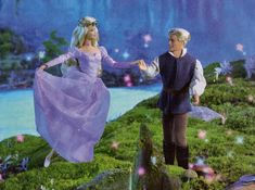 a man and woman dressed in fairy costumes standing on top of a lush green hillside