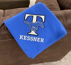 a blue towel with the letter t on it sitting on top of a brown couch