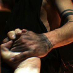 two hands holding each other with tattoos on their arms and wristbands, in front of a blurry background