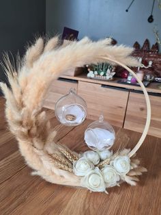 a wreath with flowers and feathers on a wooden table in front of a vase filled with white roses