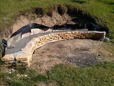 an outdoor fire pit built into the side of a hill with grass and rocks around it