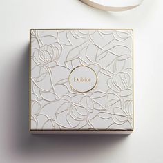 a white box with gold trim sitting on top of a table next to a ribbon