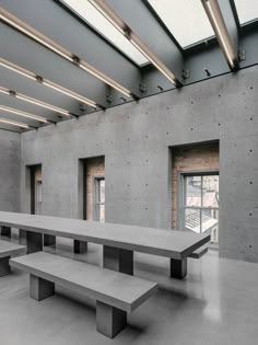 an empty concrete room with benches in the foreground and windows on the far wall