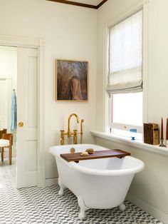 a bath tub sitting next to a window in a bathroom with a painting on the wall