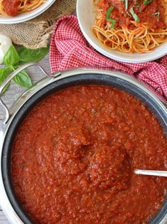 two bowls of spaghetti and one bowl of tomato sauce on a table with basil leaves