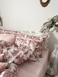 a bed with pink sheets and pillows on it next to a vase filled with flowers