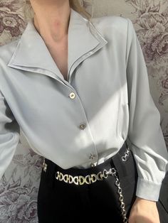 This vintage light gray blouse features a sleek, satin-like finish that gives it a refined and polished look. The blouse has a wide, structured collar and long sleeves, with minimal yet elegant buttons down the front. Its minimalist design exudes sophistication, making it a versatile piece perfect for both formal and casual outfits. The soft sheen adds a luxurious touch, making this blouse a timeless wardrobe essential. - Good vintage condition  - TAG SIZE: 42, F 44, US 14, GB 16, I 48 - Fabric Satin Chemise, Gray Blouse, Wing Collar, Double Collar, Timeless Wardrobe, Grey Blouse, Womens Shirt, Classy Women, Grey Blue