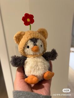 a hand holding a small stuffed animal with a flower on it's head,