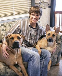 a man sitting on top of a couch with two large dogs in front of him