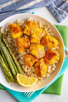 a white plate topped with rice and chicken next to asparagus on a blue napkin