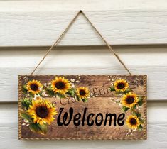 a wooden sign with sunflowers hanging on the side of a building that says welcome