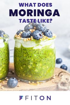 two jars filled with green smoothie and blueberries on top of a wooden board