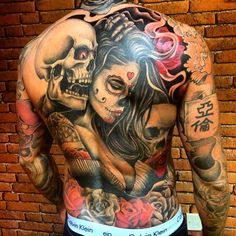 a man with tattoos on his back is standing in front of a brick wall