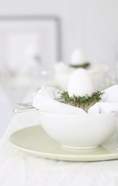 an egg is sitting in a bowl on a table with other plates and utensils