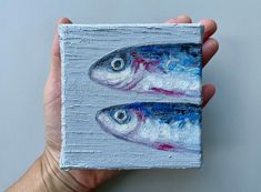 two fish painted on a piece of wood in someone's hand