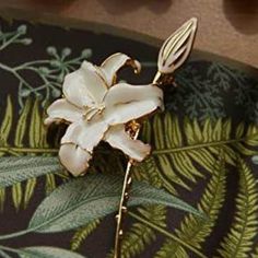 a white flower is sitting on top of a green leafy tablecloth with gold accents