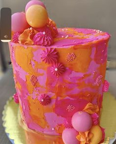 an orange and pink cake with flowers on it sitting on a yellow plate next to a knife