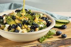 a salad with blueberries, cucumbers and cheese being drizzled over it