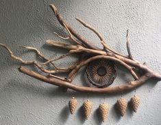 an eye made out of branches and cones hanging on the wall next to a clock