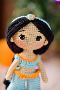 a small doll made out of crochet is sitting on a table next to an orange