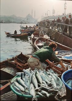 an old photo of people in boats with fish on the water and men standing around