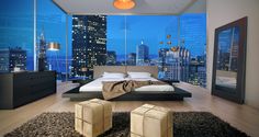 a bedroom with a large window overlooking the city at night and an ottoman on the floor