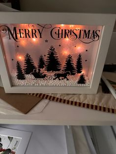 a lighted christmas scene in a white frame with trees and reindeers on the side