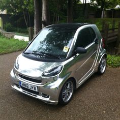 a silver smart car parked in front of some trees