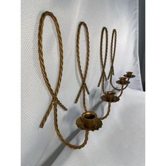 four brass candlesticks are lined up on a white cloth with rope wrapped around them