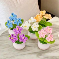 small crocheted flowers in white vases on a marble countertop next to a pillow