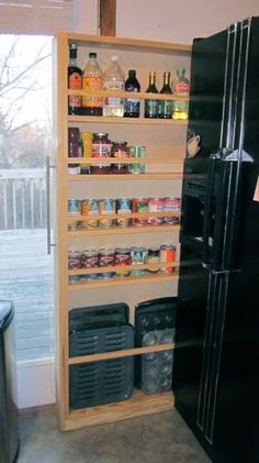 a black refrigerator freezer sitting inside of a kitchen next to a wooden shelf filled with bottles