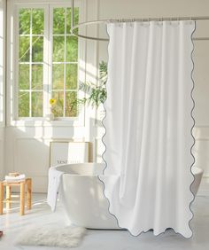 a white bath tub sitting under a window next to a wooden table with a potted plant on it