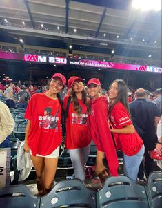 three women in red shirts and white shorts posing for the camera at a baseball game